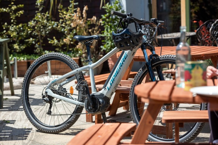 Mountain bike parked near a wooden bench outdoors on a sunny day.