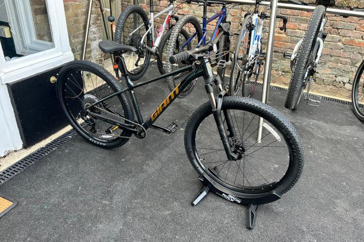 Black mountain bike on stand outside, with more bikes in the background.