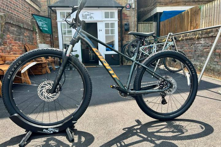 A black mountain bike displayed on a stand outside a brick building.