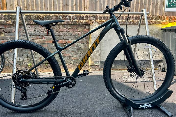 A mountain bike with a black frame and yellow accents placed on a stand.