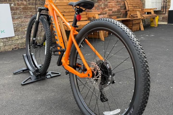 Orange mountain bike on a stand, positioned in a courtyard with brick walls.