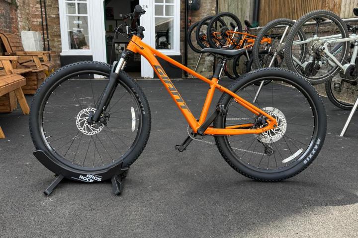 Orange mountain bike on display outside a brick building with large windows.