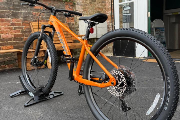 Orange mountain bike on a stand outside a bike shop.