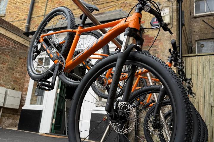 Orange mountain bikes tilted upward, parked on a street.